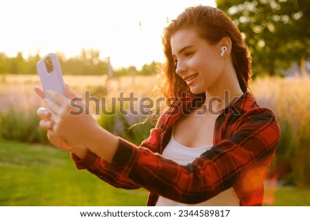 Profile photo of a happy young woman speaking via earphones and smartphone. 