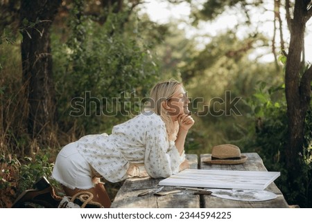 smiling woman outdoors draws a picture on a wooden table.