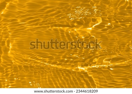 Golden water with ripples on the surface. Defocus blurred transparent gold colored clear calm water surface texture with splashes and bubbles. Water waves with shining pattern texture background.