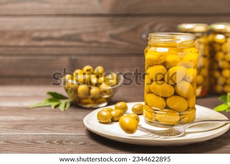 Delicious green olives. Pickled olives in glass jar. On a wooden background.Tasty olives. Close-up. Vegan.Place for text. copy space. Royalty-Free Stock Photo #2344622895
