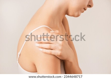 profile of a young woman in white underwear, suffering from bursitis, experiencing acute pain in the shoulder joint. Shoulder injury. Isolated on a beige background. Royalty-Free Stock Photo #2344648717