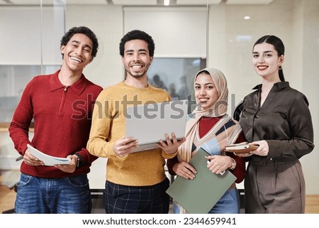 Waist up portrait of Middle Eastern business team standing in modern office and smiling at camera cheerfully holding computers and documents Royalty-Free Stock Photo #2344659941
