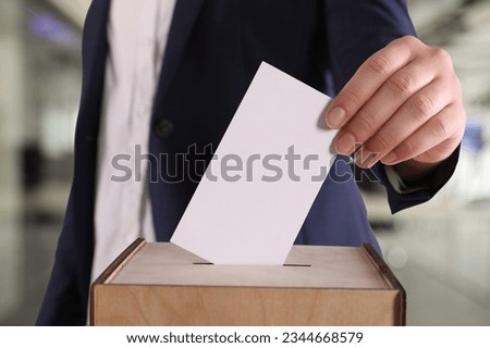 Woman putting her vote into ballot box on blurred background, closeup Royalty-Free Stock Photo #2344668579