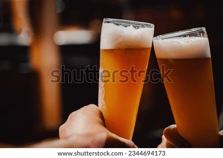 Two friends hands clinking glasses of craft beer at the pub or bar Royalty-Free Stock Photo #2344694173