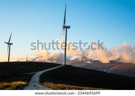 Conceptual photo background of tranquility at sunset. A wind farm with wind turbines in the mountains with snow and clouds. Calm sunset light and for wallpapers on your computer or phone