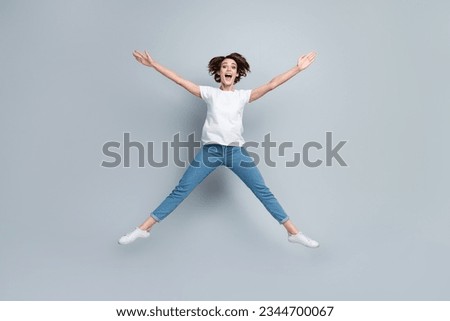 Full size photo of astonished ecstatic girl dressed white t-shirt jeans jumping like star hands up isolated on gray color background