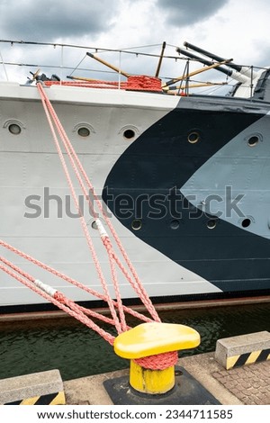 Painted gray - camouflage - the side of a warship, thick orange ropes mooring to the quay, sailor