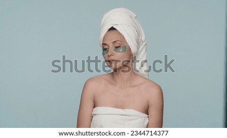 Woman wrapped in bath towels after a shower on a blue background. Portrait of a woman with green hydrogel patches under her eyes close up. The concept of beauty, cosmetology, skin care.
