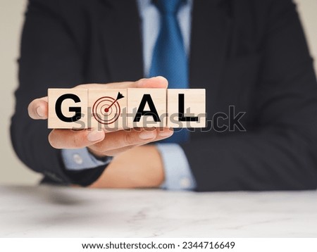 Business planning strategy concept. A Businessman holding wooden cubes with the letters GOAL and dartboard icon while sitting in the office. Achieve on-point, sustainable challenge goals.