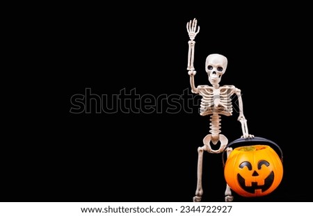 A human skeleton greeting, waving, holding a Halloween orange pumpkin on a black background. Halloween Greeting Card