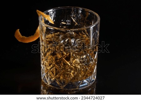 Glass of wiskey with ice cube and orange peel on black reflective background 
