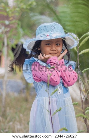 Kulon Progo, Indonesia August 08, 2023,a beautiful and cute little girl poses wearing a hat and cotton summer dress in a village near Kulon Progo City in the afternoon