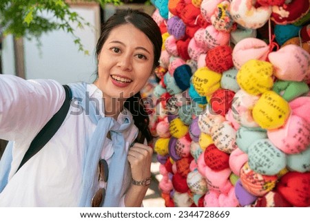 happy asian Japanese girl tourist looking at camera with smile while taking self portrait photo with colorful cloth ball ema at Yasaka Koshin-do kongoji temple in Kyoto japan