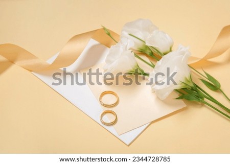 Wedding rings, card, ribbon and eustoma flowers on color background