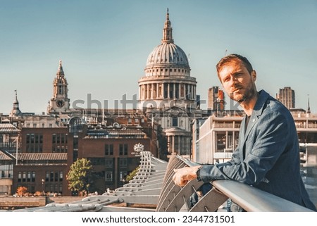 Young man leaning on railing of Millennium bridge. Male tourist looking away during vacation. Cathedral of St. Paul Church with clear blue sky in background on sunny day.