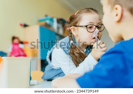 Integration of children with special needs concept. Little girl with down syndrome using dentist tool on boy as patient at school or kindergarten. Royalty-Free Stock Photo #2344739149
