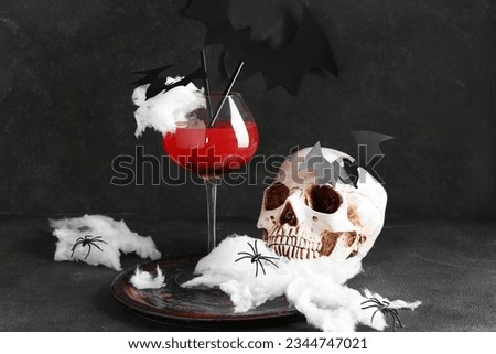 Glass of tasty Margarita cocktail, skull and decorations for Halloween on black background