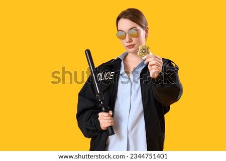 Female police officer with baton and badge on yellow background Royalty-Free Stock Photo #2344751401