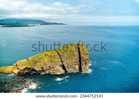 Volcanic rock and lonely sailing boat in the calm blue waters of the Atlantic Ocean, cloudy sky during sunny summer day. Sao Miguel Island, Ponta Delgada, Azores. Portugal  Royalty-Free Stock Photo #2344752141
