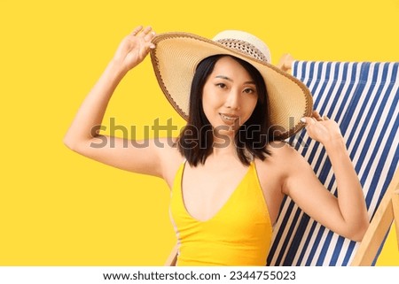 Beautiful Asian woman relaxing in deck chair on yellow background