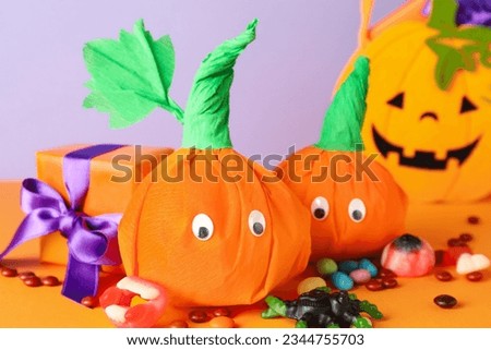 Paper pumpkins for Halloween, gift box and tasty candies on color background, closeup