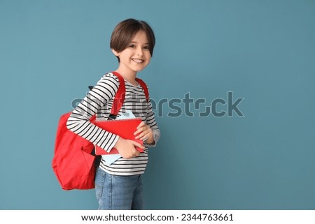 Happy little boy with backpack and notebooks on blue background