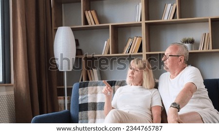 A European elderly couple is relaxing at home on the sofa, they are talking to each other.