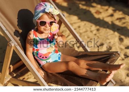 Funny cute girl on summer vacation. The child has fun on the beach. Cute baby girl in a colorful swimsuit and sunglasses is resting and eating ice cream.