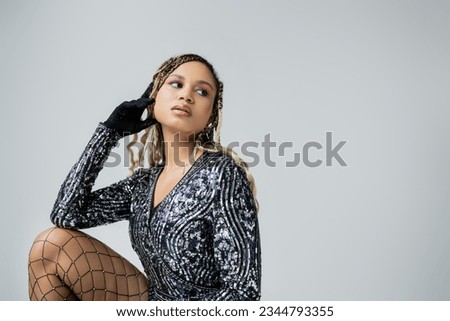 portrait of african american woman in shiny blouse looking away, grey background, fashion and style