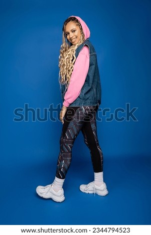 happy african american woman with hood on head posing in sporty outfit on blue background, joy