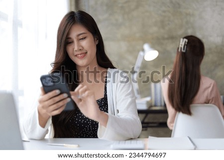 Female saleswoman in office using smartphone to send text messages online and using mobile phone to talk to customers.