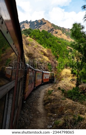 train on track along side trees and mountains with cloudy sky in the background.