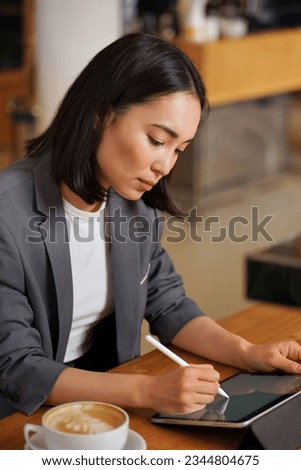 Busy young professional Asian business woman using applications on digital tablet sitting at table remote working or learning online, holding stylus writing e signature signing electronic document.