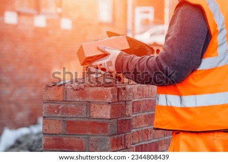 Hard working bricklayer lays bricks on cement mix on construction site. Fight housing crisis by building more affordable houses concept