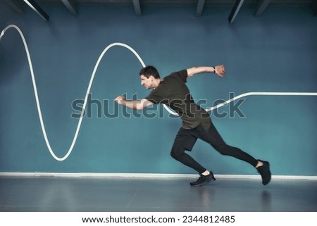 Great shape. Full length of young athletic man in sport clothing running against blue wall while exercising at gym