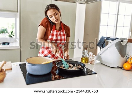 Young beautiful hispanic woman talking on smartphone cooking at the kitchen Royalty-Free Stock Photo #2344830753