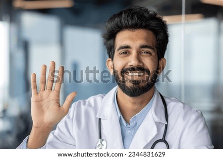 Portrait of a young smiling Indian male medical student in a white coat waving, greeting and smiling at the camera. Close-up photo.