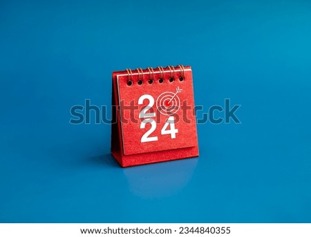 Happy new year 2024 banner background. 2024 numbers year with target dart icon on red small desk calendar cover standing on blue background, minimal style. Business goals plan and success concepts. Royalty-Free Stock Photo #2344840355