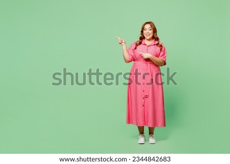 Full body smiling cheerful fun young chubby redhead woman wear casual clothes pink dress point index finger on area copy space isolated on plain pastel light green color background. Lifesyle concept