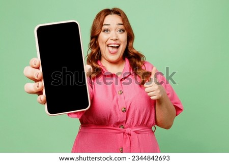 Young fun chubby overweight redhead woman wear casual clothes pink dress hold in hand use close up blank screen workspace area mobile cell phone show thumb up isolated on plain green color background