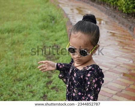 Cute child portrait image of eyeglass. Little girl clear face focusing at camera. Dress wearing black and designing. Glorious look with close up hand style behind blur background.