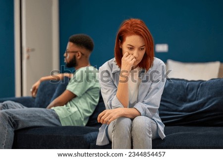 Communication problems in marriage. Upset diverse family couple european wife and african american husband sit separately on sofa at home not talking after fight, having problems in relationships.  Royalty-Free Stock Photo #2344854457