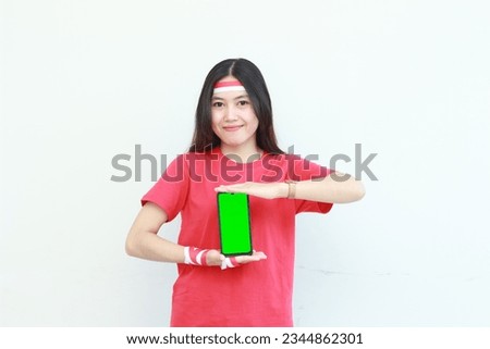 portrait of beautiful asian woman wearing red outfit celebrating Indonesia independence day by gesturing holding mobile phone isolated on white background.