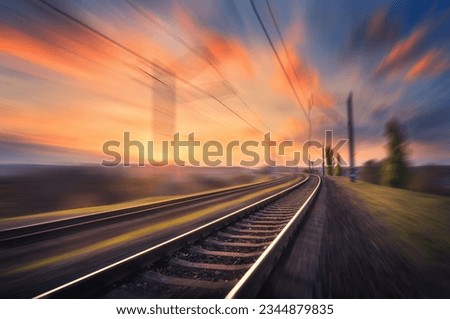 Railroad in motion at sunset. Railway station with motion blur effect against colorful blue sky, Industrial concept background. Railroad travel, railway tourism. Blurred railway. Transportation Royalty-Free Stock Photo #2344879835