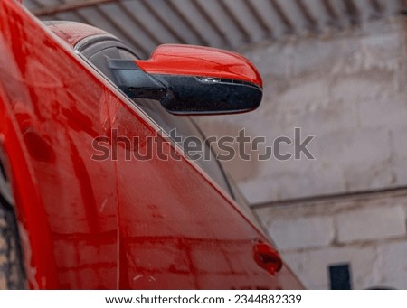 This close-up shot of a dusty red car in a garage highlights the car's weathered exterior and dirty side mirror