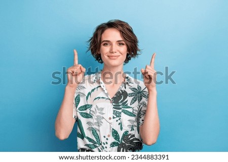 Photo portrait of attractive young woman fingers pointing up empty space wear trendy print leaves clothes isolated on blue color background