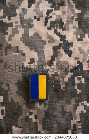 Vertical photo of banner of ukrainian flag on camouflage textile with military pixel colors.