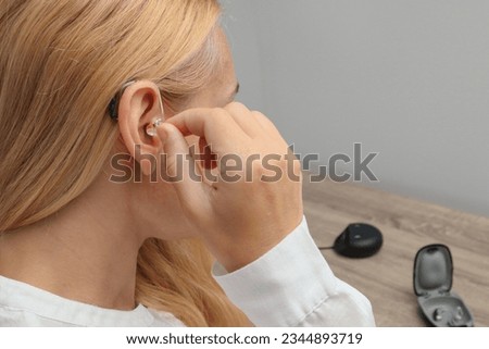 Close up of Woman inserting her hearing aid into ear. Blonde Woman with Modern Hearing Aid. Hearing Impaired. Royalty-Free Stock Photo #2344893719