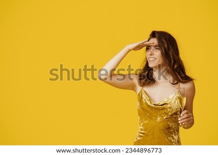 Happy lady in cocktail dress enjoying holiday, holding champagne glass and looking aside at copy space over yellow studio background. Birthday, bachelorette party, new year and holiday celebration