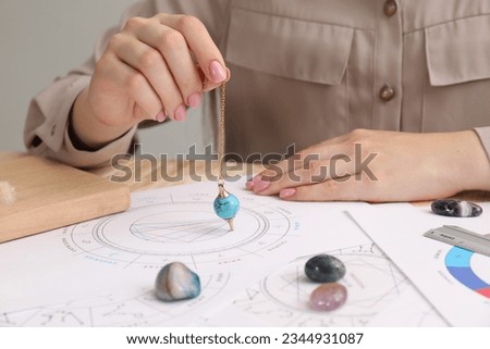 Astrologer using natal chart and pendulum for making forecast of fate at table, closeup. Fortune telling Royalty-Free Stock Photo #2344931087